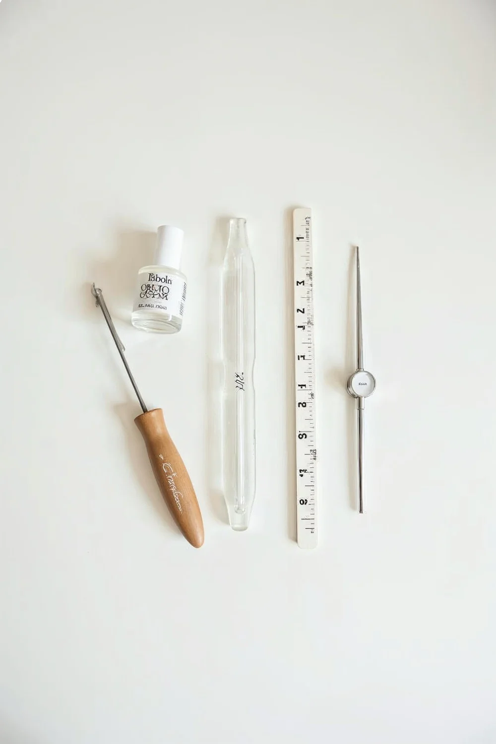Flat lay of almond filing tools including a glass file, buffer, cuticle oil, base coat, and measuring guide on a clean surfac