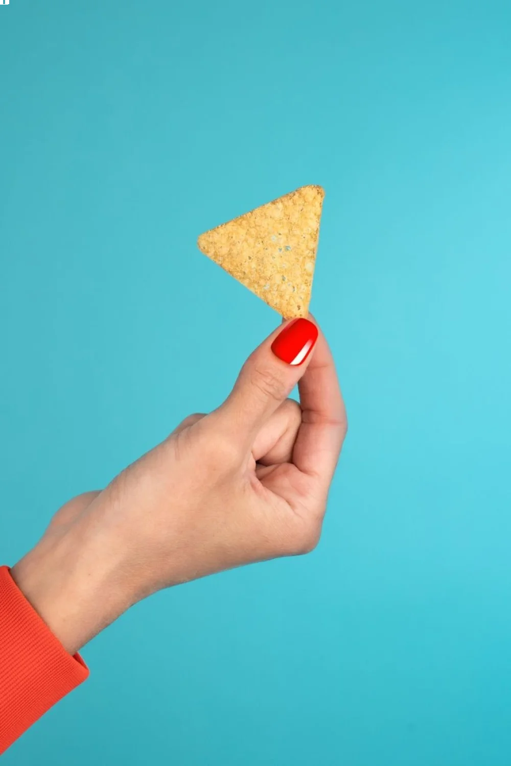 Coral pink nails with white tips holding a triangular tortilla chip against a blue background