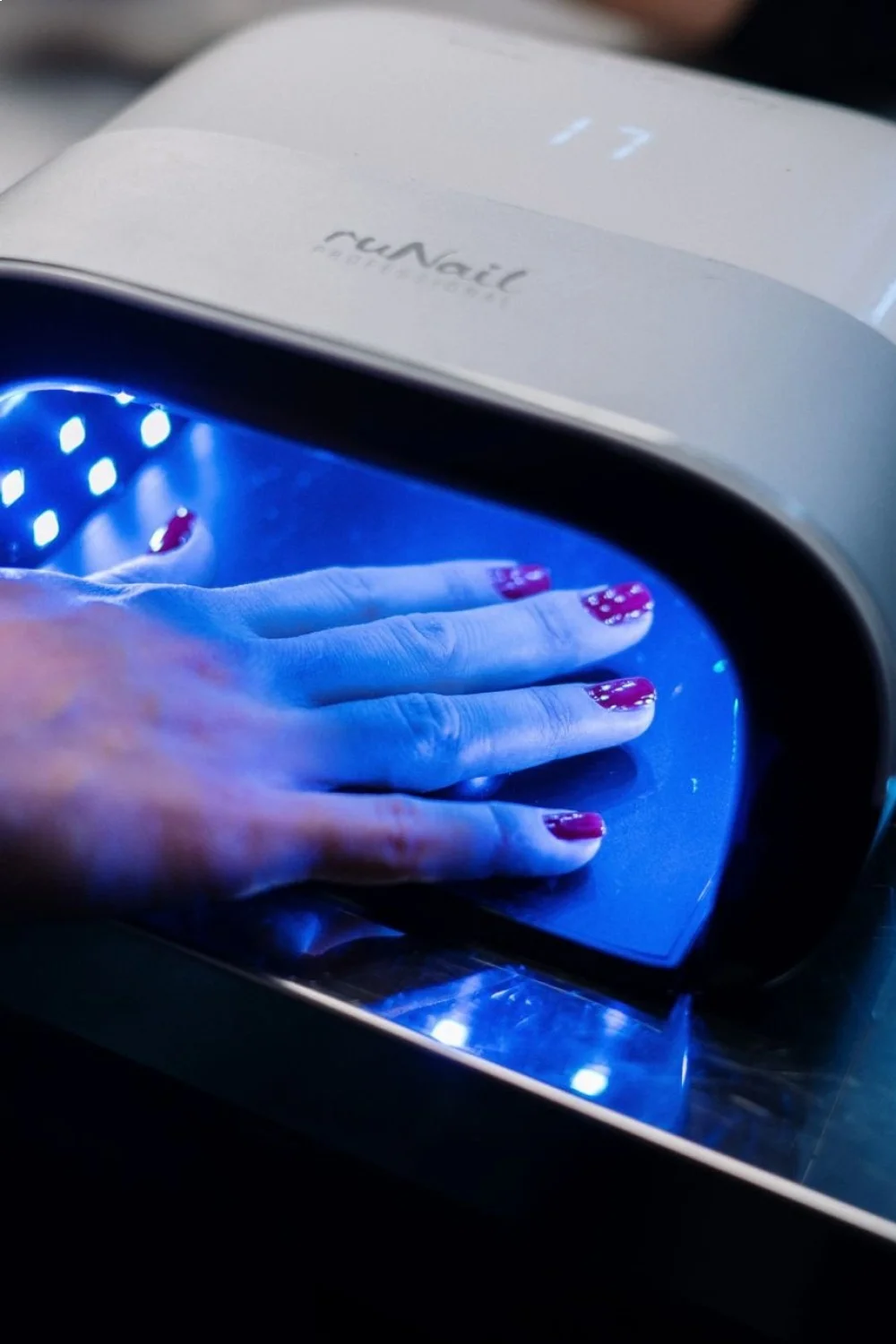 Coral pink nails with polka dot accent design curing under a UV lamp for back to school nails