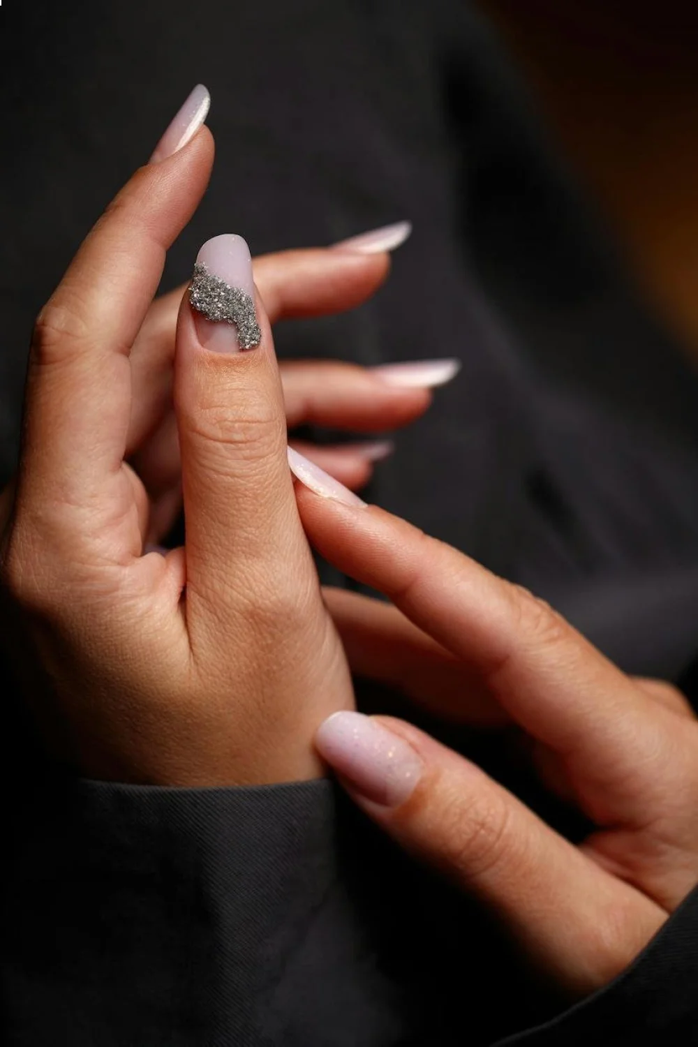 Hand displaying beach nails with nude shades and a micro seashell accent on the ring finger