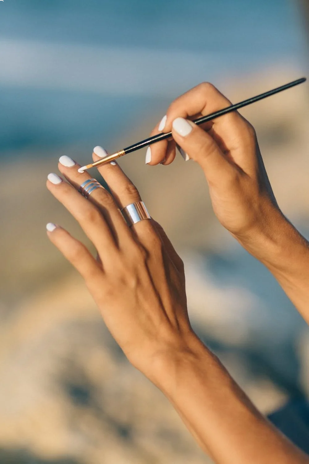 coral pink french tips with gold accents on almond nails being painted by a hand holding a fine brush