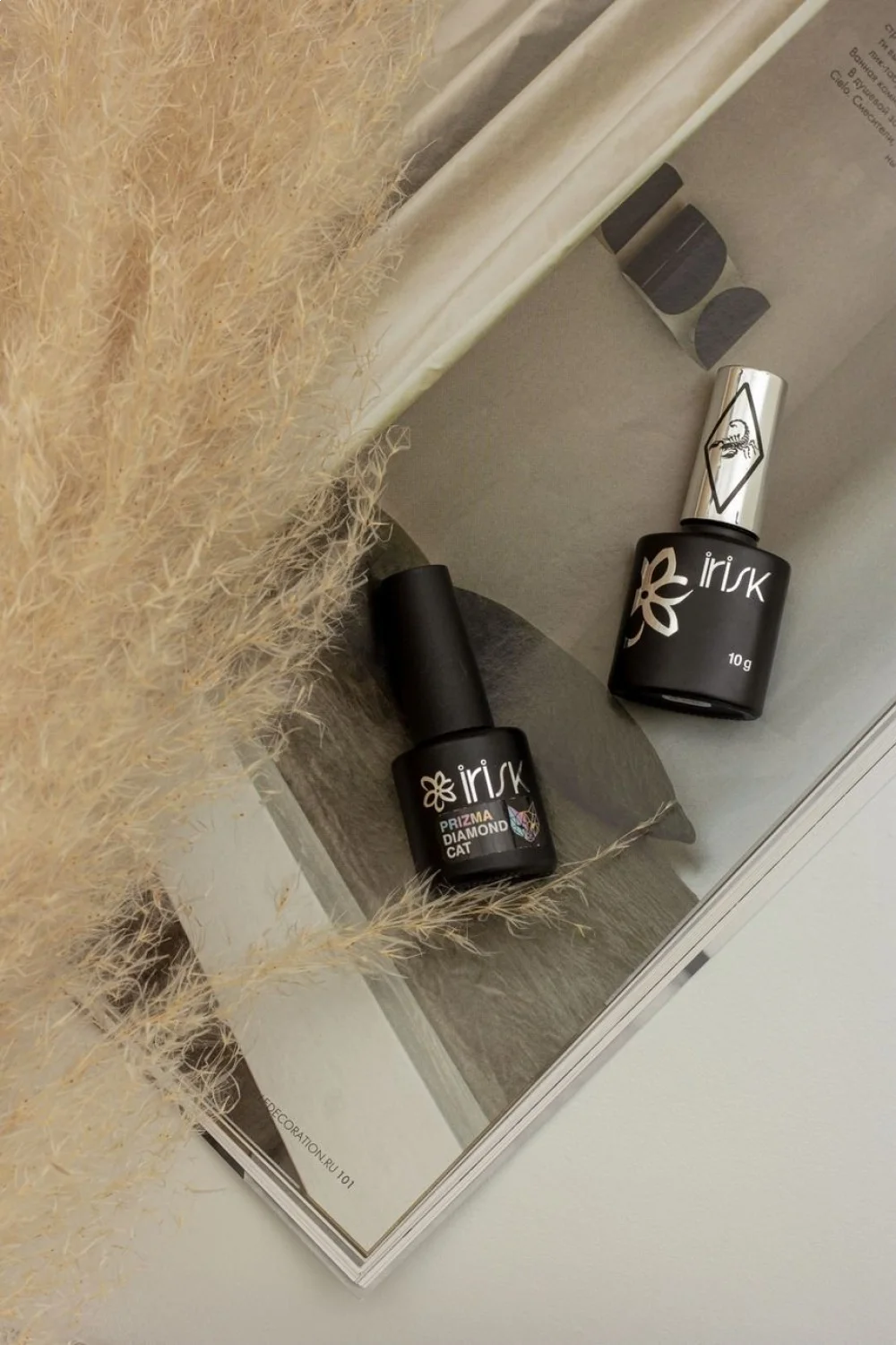 Two gel polish bottles on a magazine page with soft beige pampas grass in the foreground