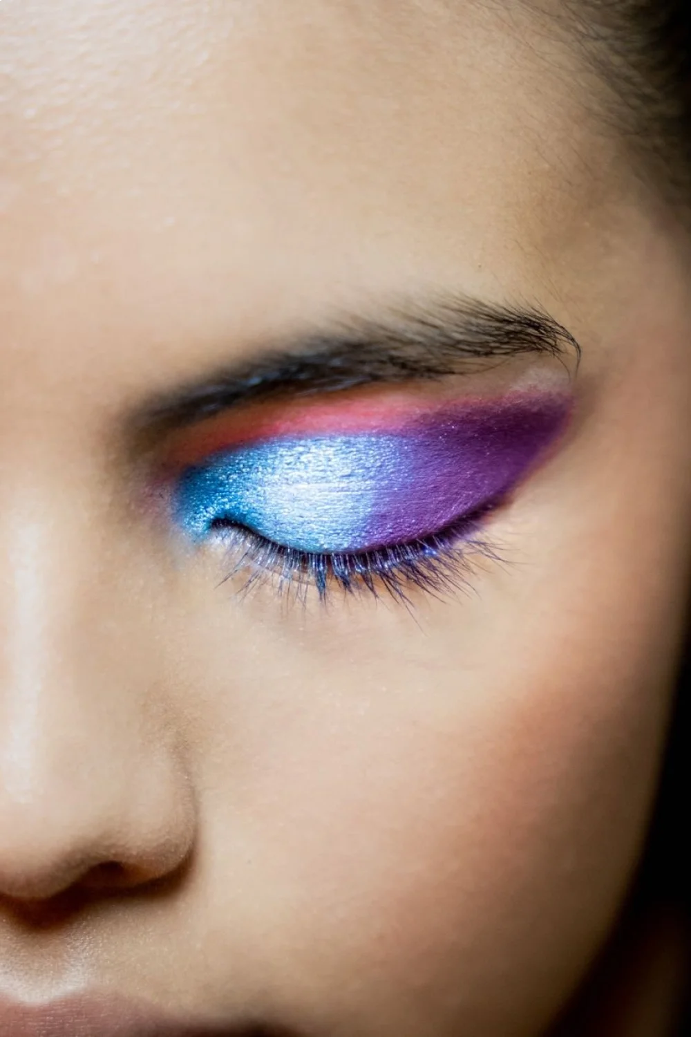 Close-up of a woman's eye with vibrant blue, purple, and pink gel polish on eyelids