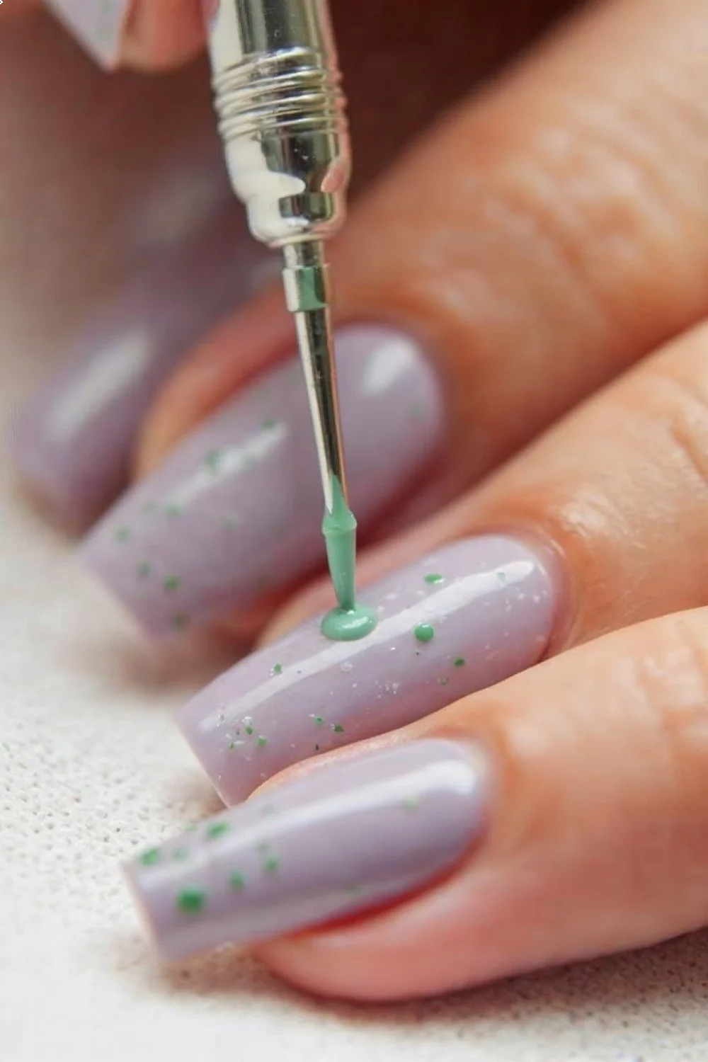 Close-up of spring nail art in progress showing dotting tool creating sage green dots on lavender base