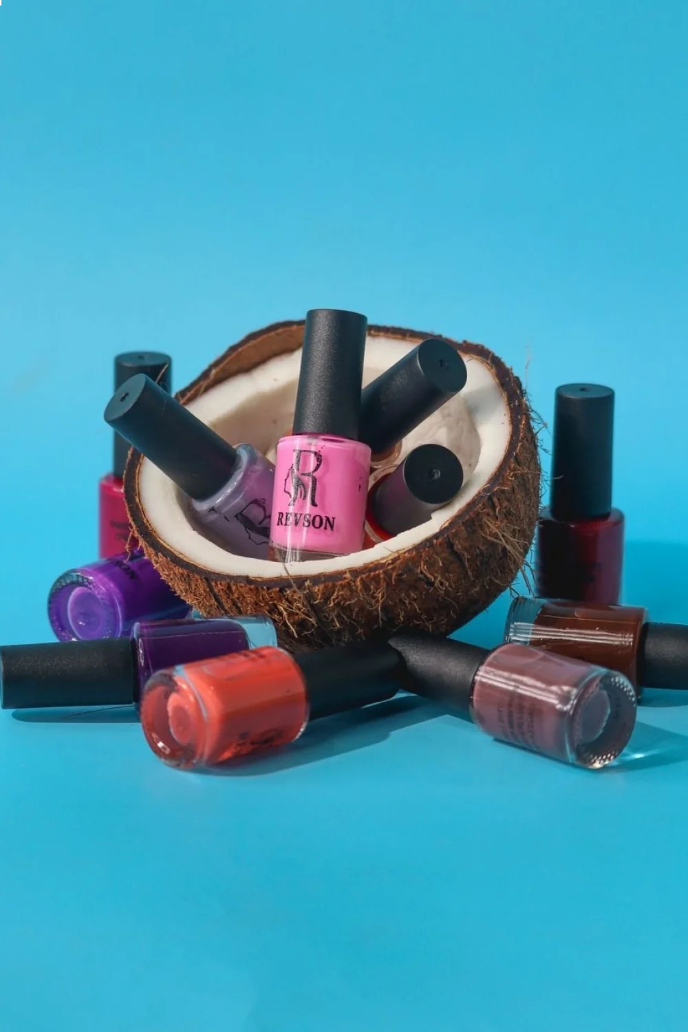 15 nail polish bottles in coral to turquoise gradient with applicator brushes arranged around a coconut shell