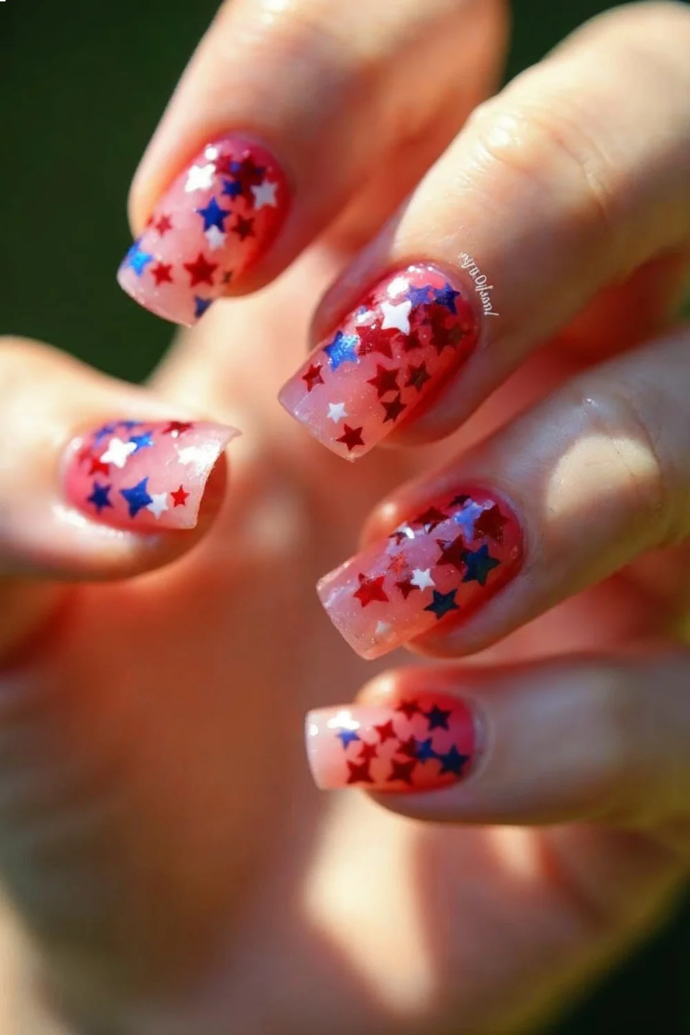 Red, white, and blue star confetti on sheer pink base, nails at a slight angle, top coat applied, fourth of July nails