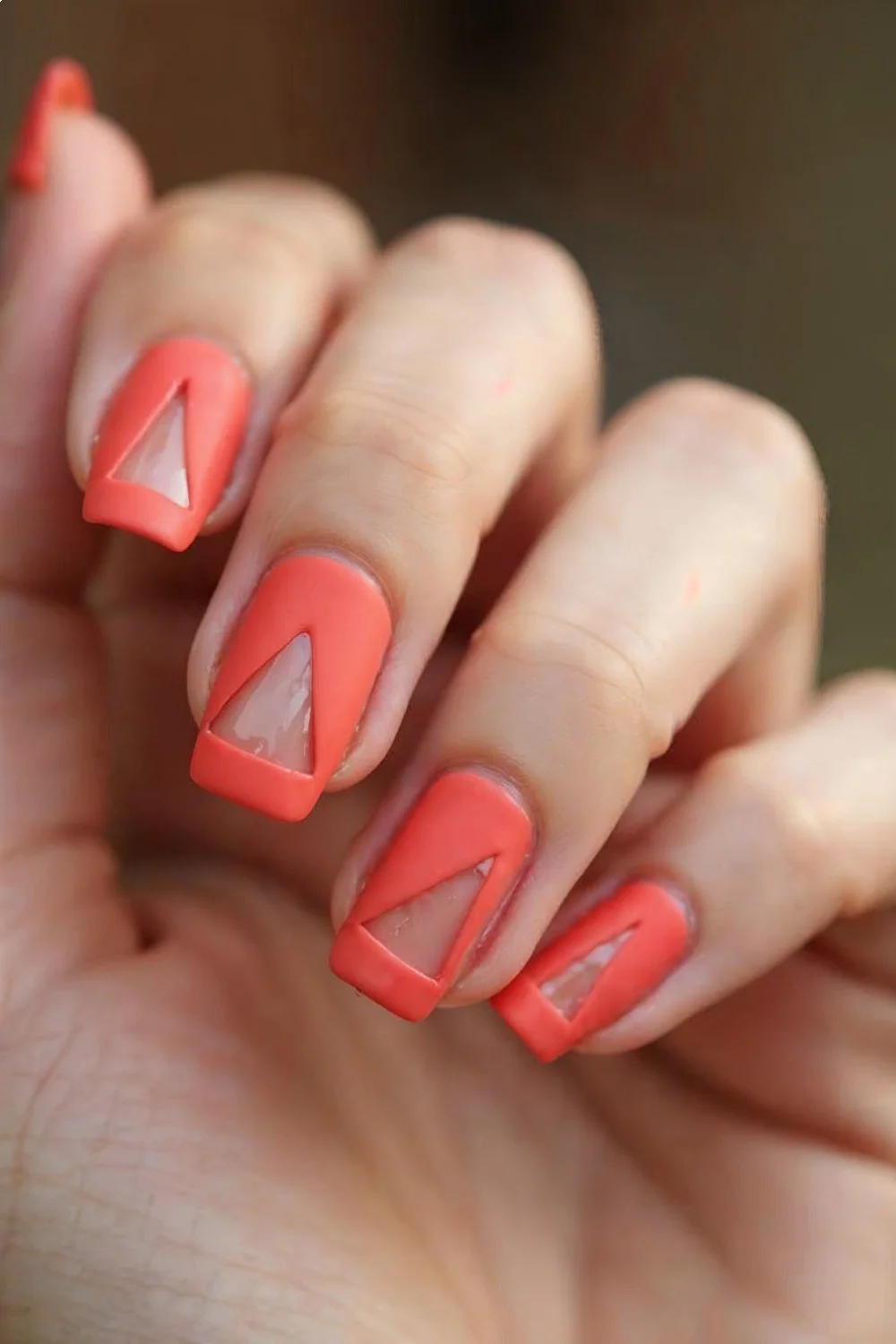 Nude nails with matte coral geometric sections and triangular negative space at the cuticle in a matte nail designs style