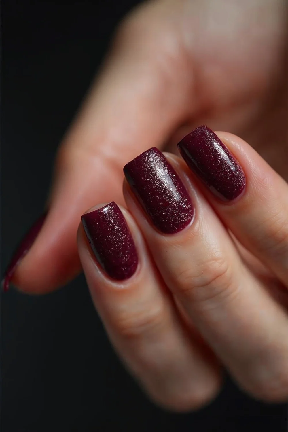 Textured matte burgundy nails with visible sparkle particles on a hand