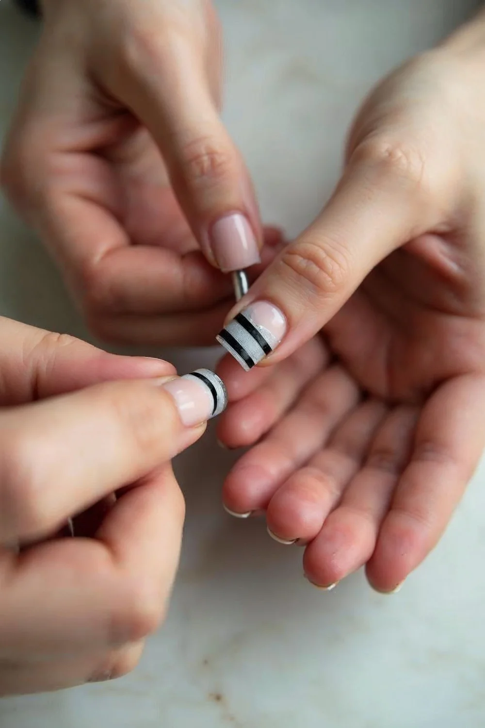 Coral pink matte nails with black geometric stripes being applied with tape technique