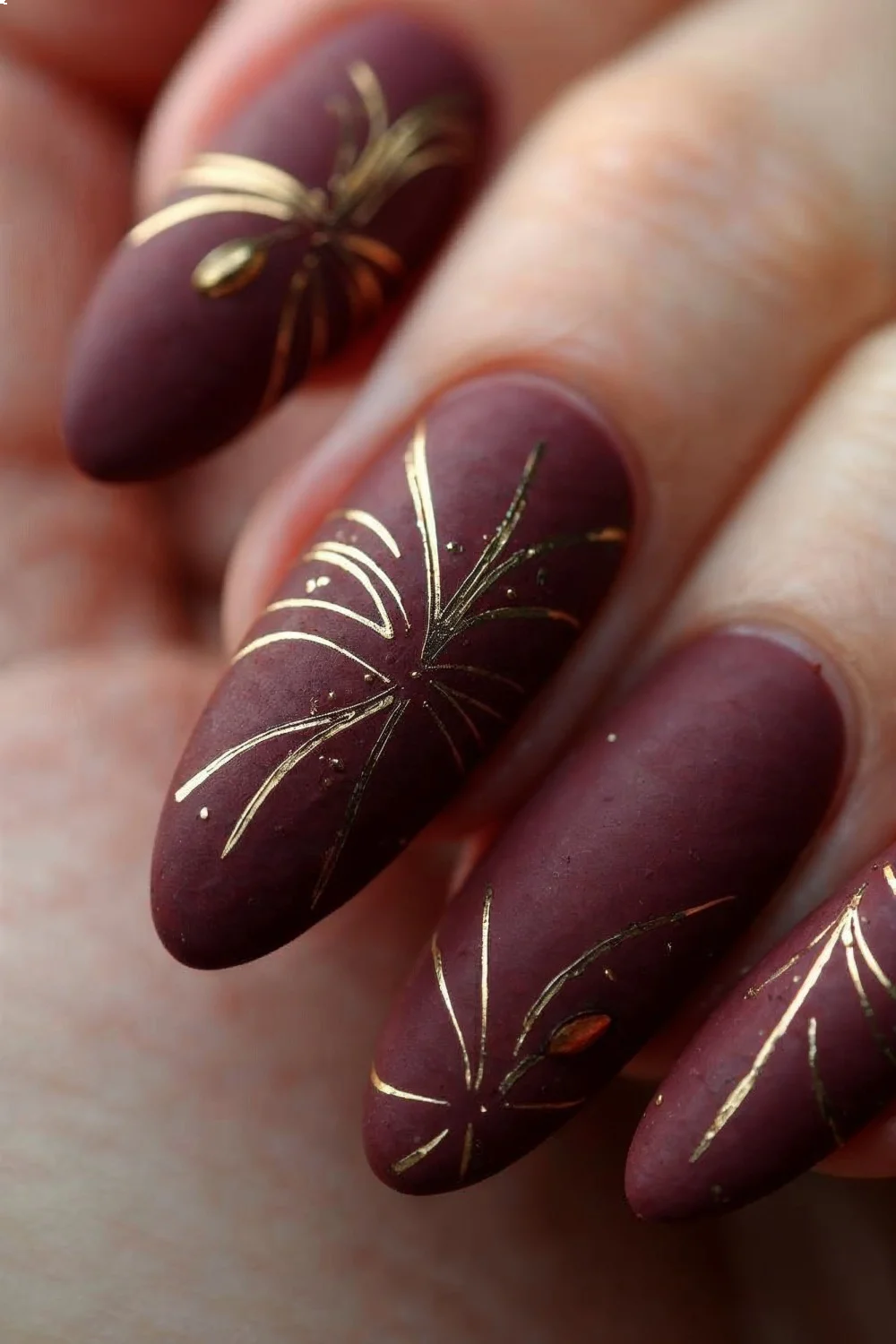 deep burgundy matte nails with fine gold line art designs on almond-shaped tips