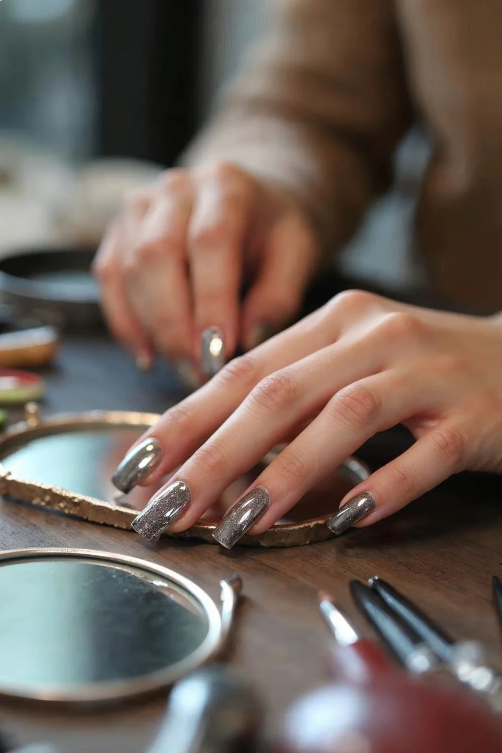 Close-up of chrome powder nails showing mirror reflection and application tools arranged on desk