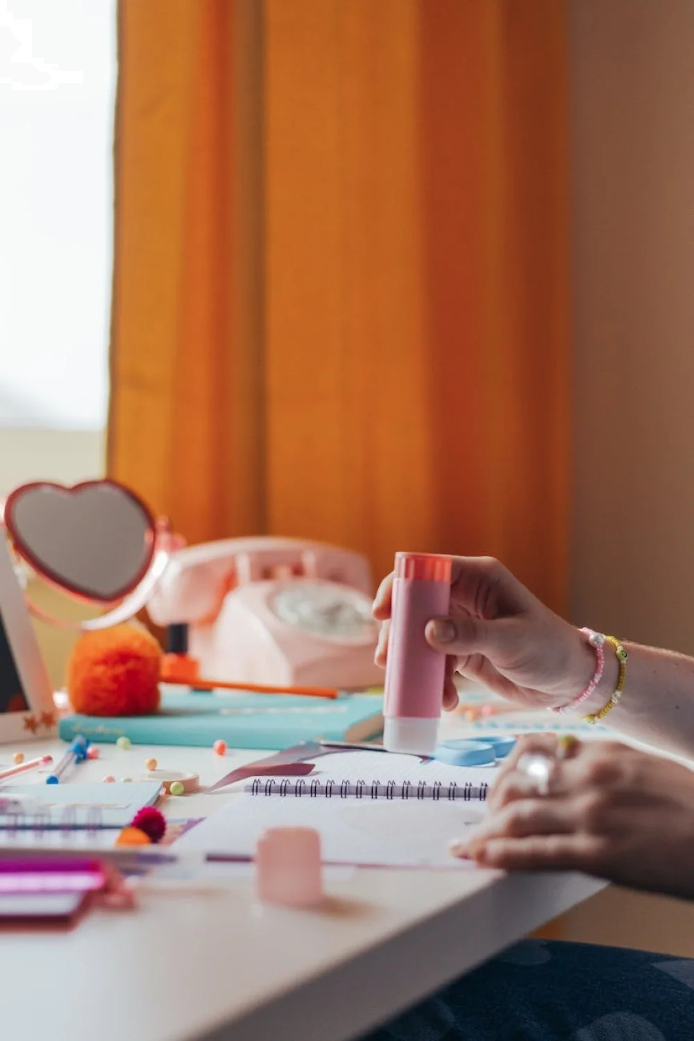 Hand applying glue to a natural nail with a pink applicator, surrounded by colorful nail art supplies