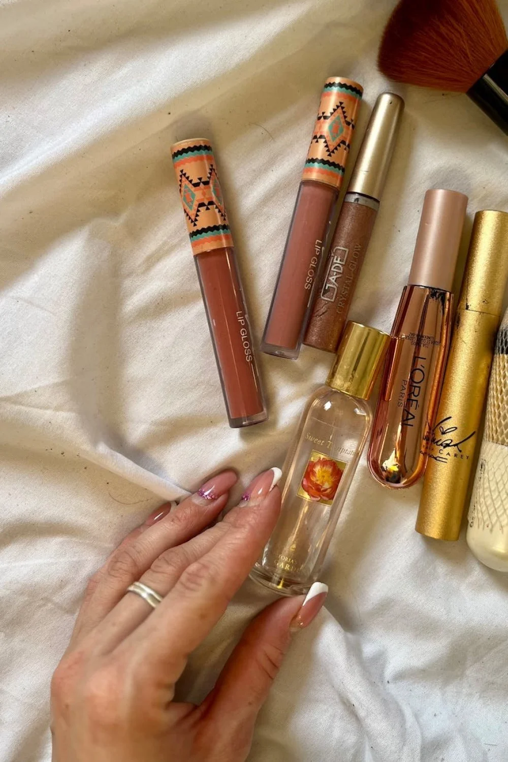 coral pink french tips with gold accents on almond nails beside lip glosses and a perfume bottle