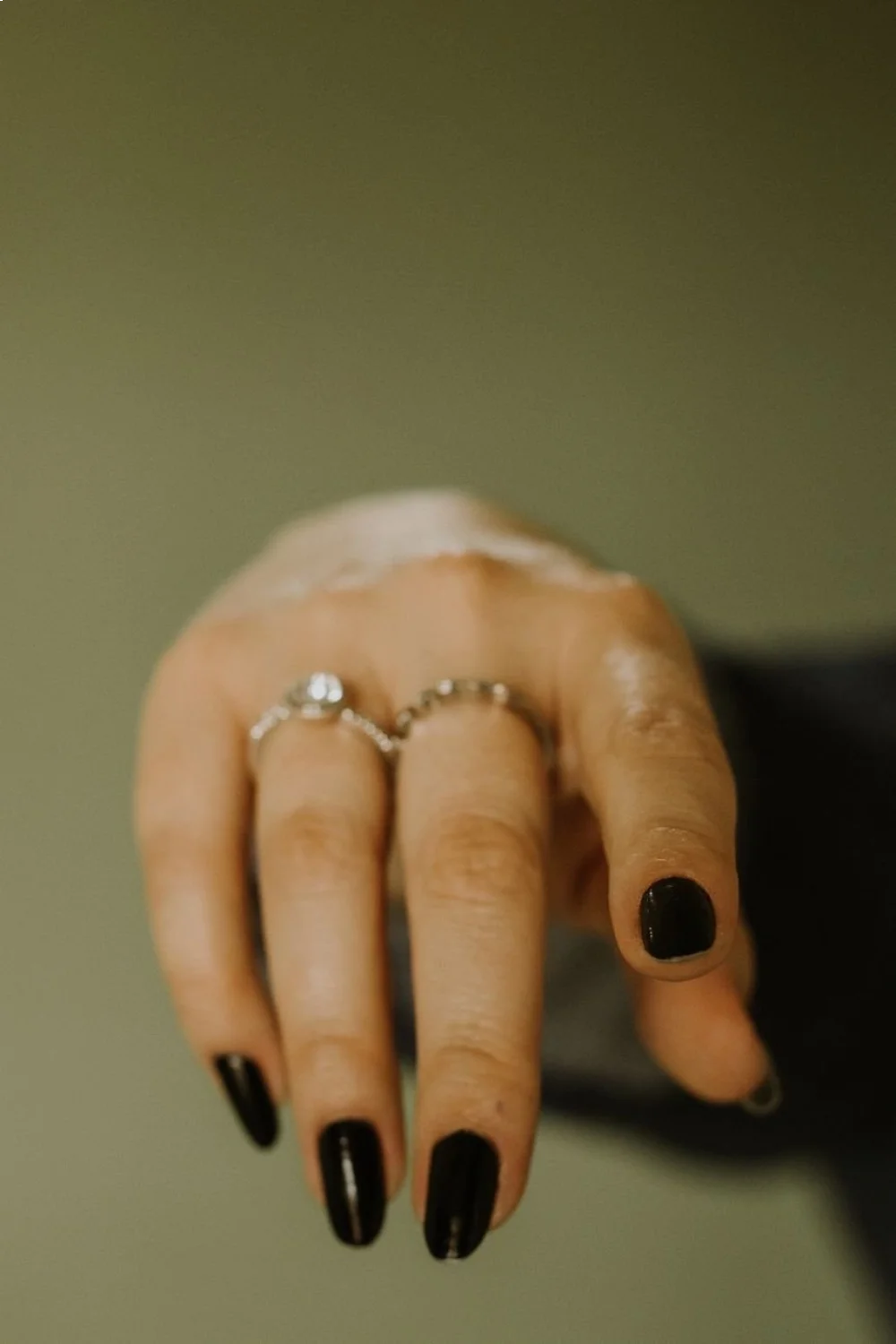 Close-up of a hand with black squoval nails, adorned with silver rings against a soft background