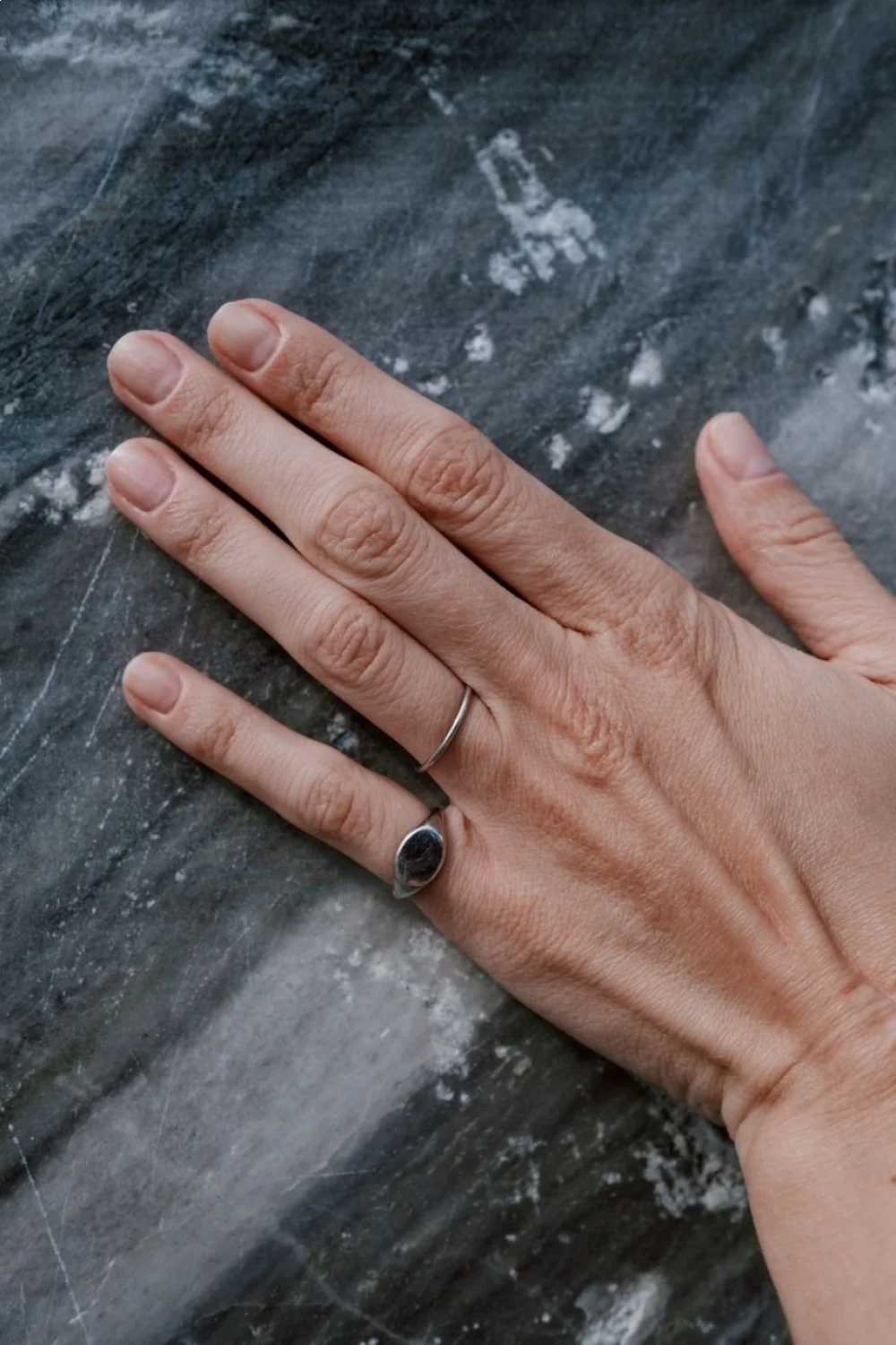 Hand resting on a textured gray surface with squoval nails in a natural nude shade