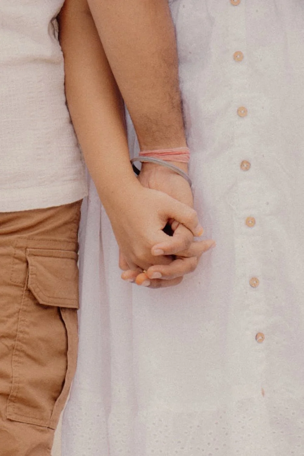 Two hands holding each other, one with sunset nails in orange to pink gradient and the other in coral to purple gradient