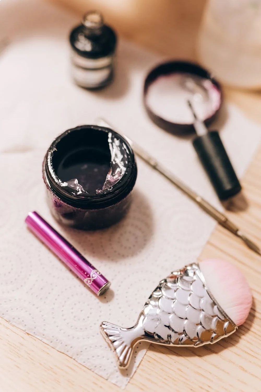 uncured gel colors in a black jar, nail brush, and a pink brush on a paper towel with a nail art tool
