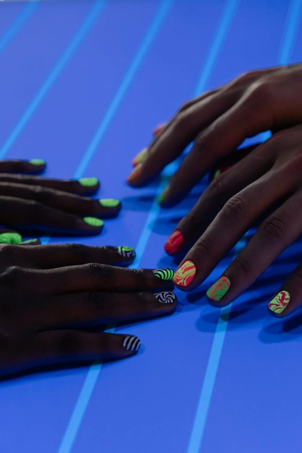Four nails in sunset colors: bright orange-pink, peachy-rose, purple-mauve, pale yellow-lavender