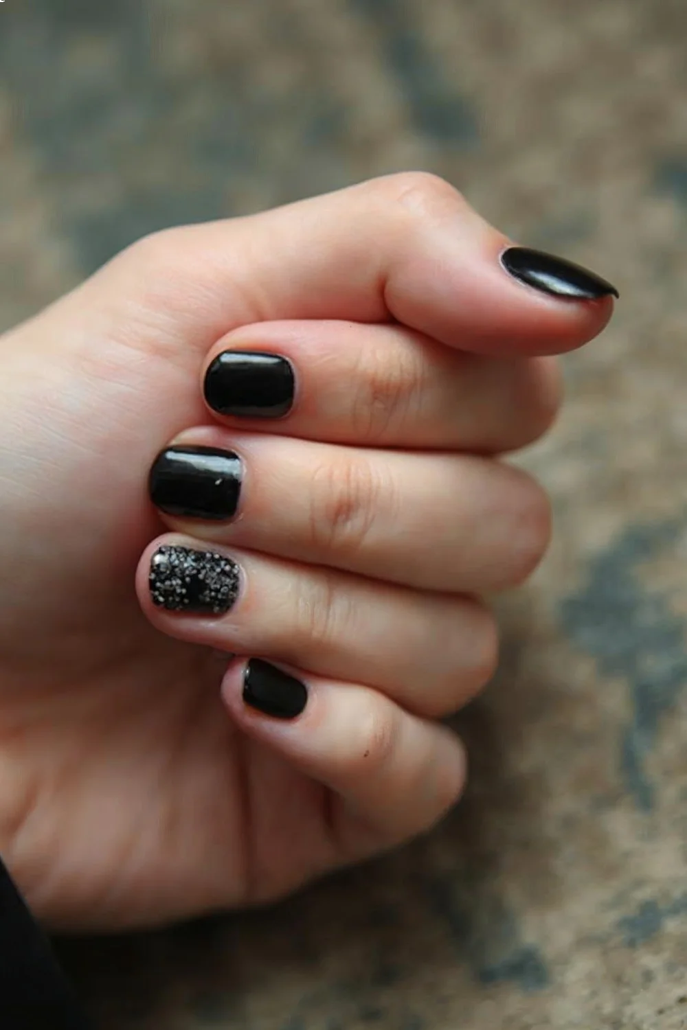 Short, rounded nails with dark gel polish and a glitter accent on one finger, ideal for vacation nails